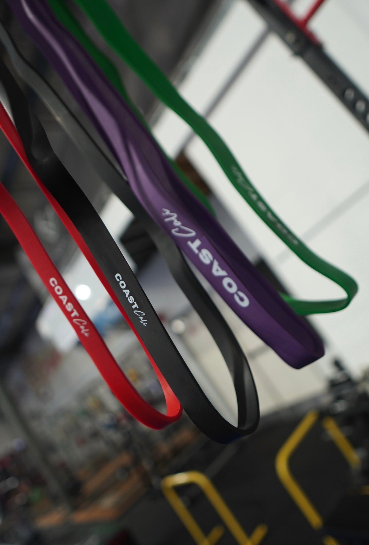 A set of 4 calisthenics resistance bands with 'Coast Cali' logo and gym in background