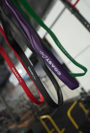A set of 4 calisthenics resistance bands with 'Coast Cali' logo and gym in background