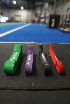 A set of 4 calisthenics resistance bands with 'Coast Cali' logo and gym in background